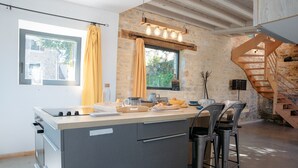 A modern kitchen with a central island, a built-in oven, and a stone accent wall. - In the heart of the village, house for 8 with pool (Coly)