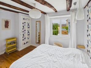 Ein Schlafzimmer mit einem Bett, einem Fenster mit Blick, einem Spiegel und einem gelben Regal.