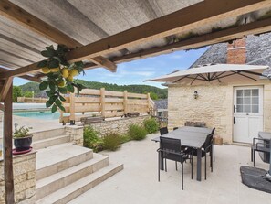 Une terrasse extérieure couverte avec une piscine, des marches en pierre et une table avec des chaises.