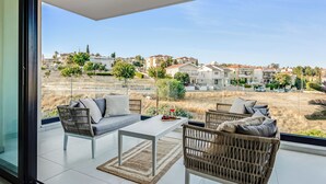 A balcony with wicker furniture, a glass door, and a view of a residential area. - Three-bedroom Penthouse With two Large Balconies (Limassol)