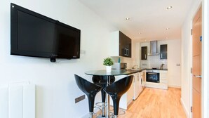 Una cocina moderna con un televisor de pantalla plana, un comedor con dos sillas y una pequeña planta en maceta.