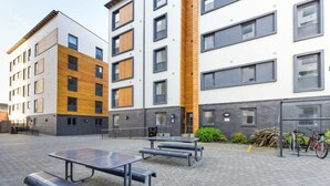 Un patio con mobiliario exterior, un aparcamiento para bicicletas y un edificio con fachadas de madera y ladrillo.