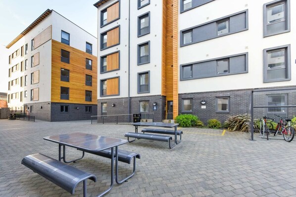 A courtyard with outdoor seating, a bike rack, and a building with a mix of wooden and brick facades.