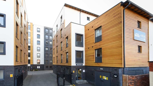 Un edificio moderno con zona de recepción, varias ventanas y entrada protegida por un portón.