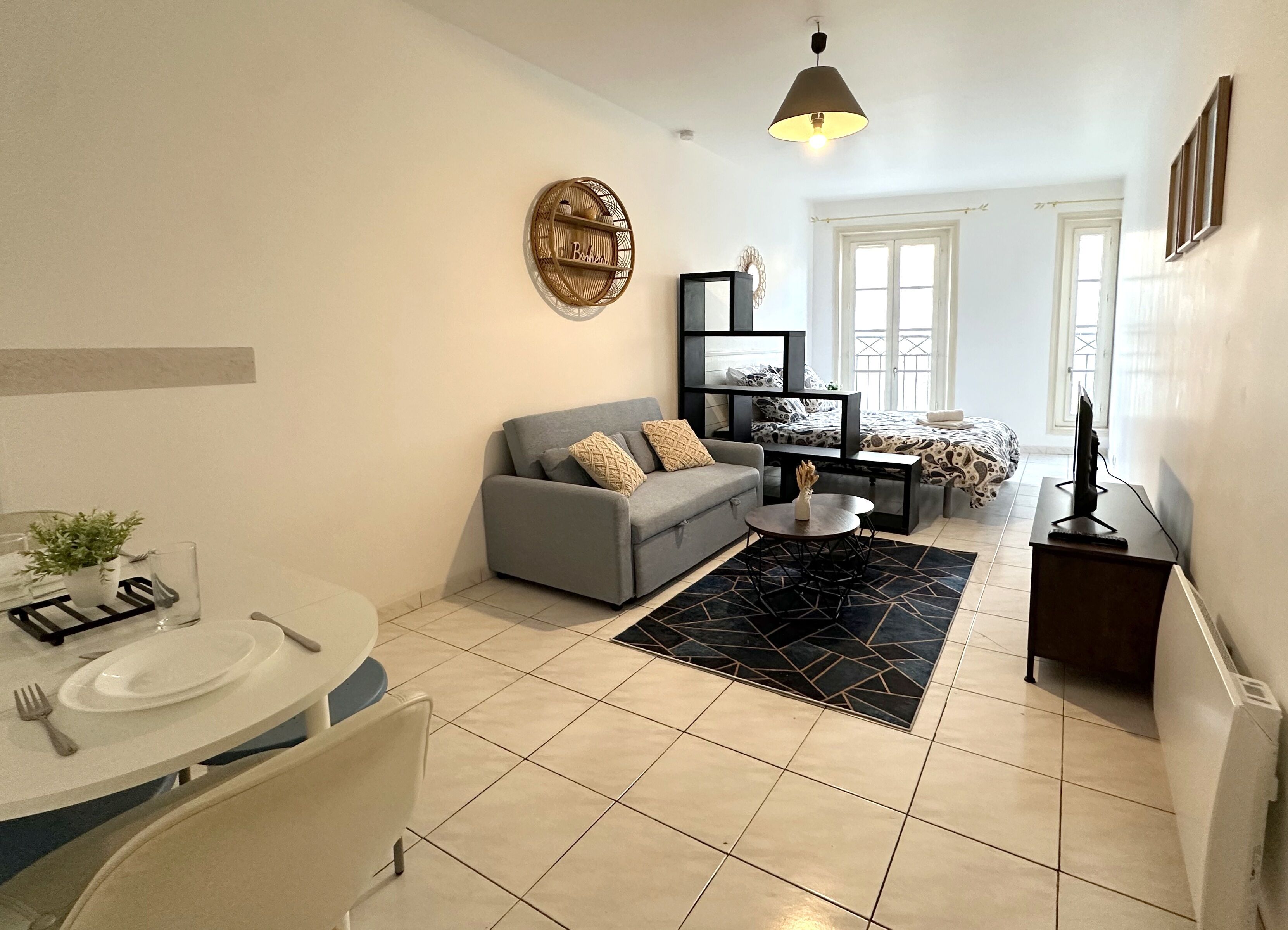 Ein modernes Wohnzimmer mit einem grauen Sofa, einem Esstisch mit Stühlen, einem Couchtisch und einem Fernseher auf einem Schrank.