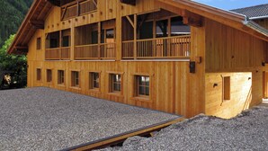 A multi-story wooden building with balconies, large windows, and a gravel driveway. - Vacation apartment "Tischlerhof Stadl" (St.Jakob/Ahrntal)