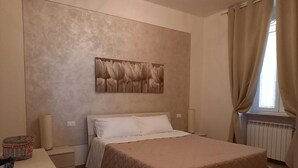 Un dormitorio con cama, mesita de noche, lámpara, radiador y ventana con cortinas.