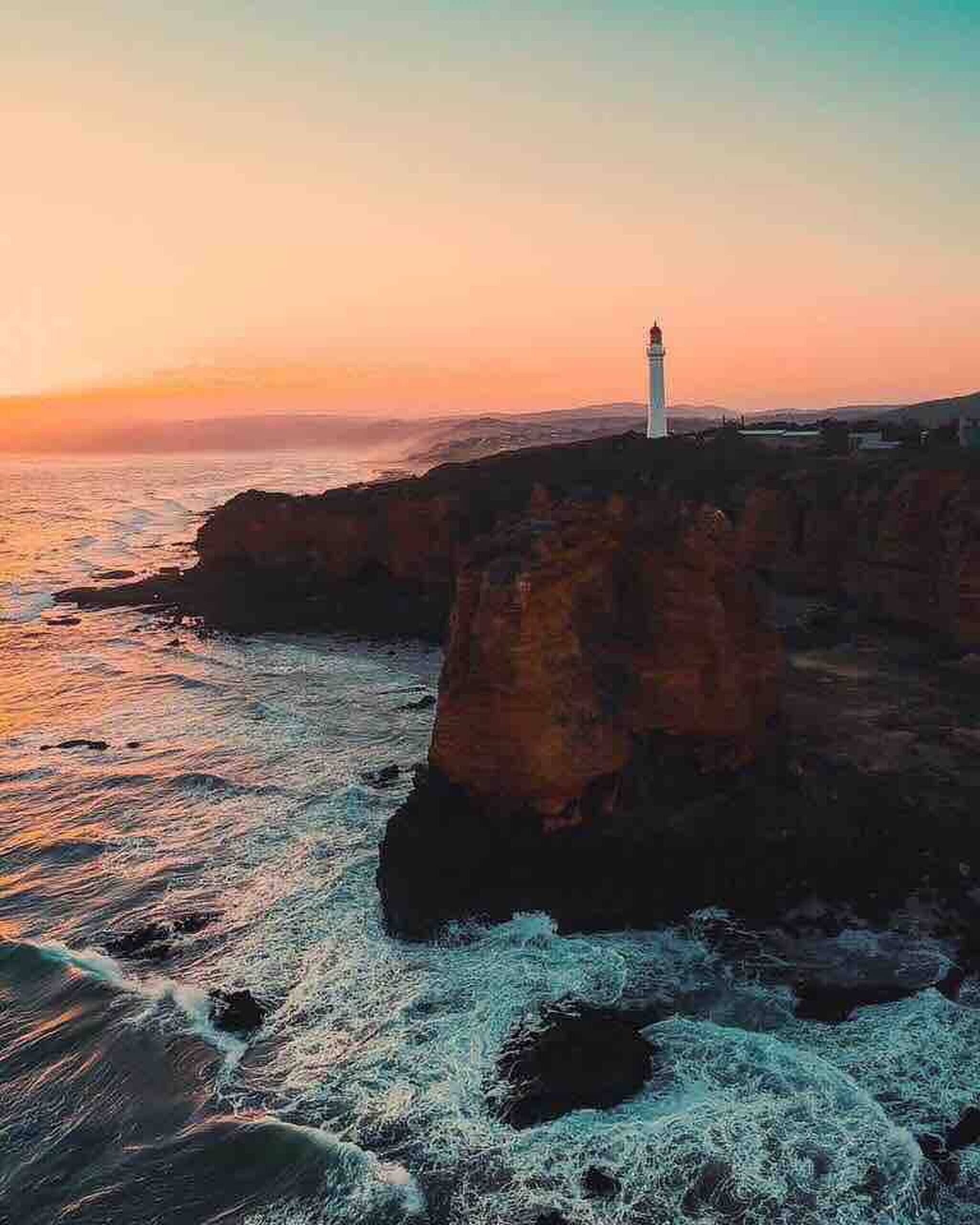 Un faro sobre un risco escarpado al borde del mar durante el atardecer.