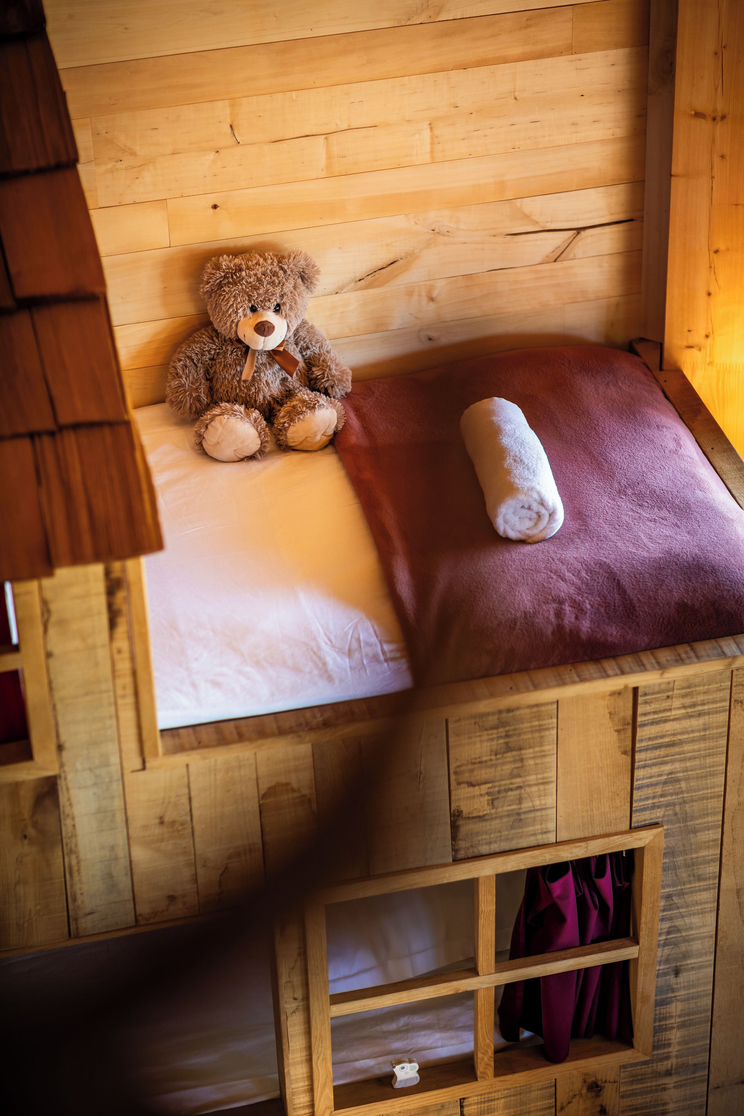 Una cama litera de madera con un oso de peluche en la parte superior y una toalla enrollada en la inferior.