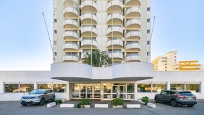A multi-story hotel with a central entrance, two cars parked in front, and a clear sky. - Praia da Rocha/1605/Charming Apart/Sea View/by IG (Portimão)