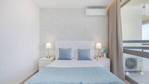 A hotel room with a bed, two bedside lamps, a window with curtains, and an air conditioning unit. - Praia da Rocha/1605/Charming Apart/Sea View/by IG (Portimão)