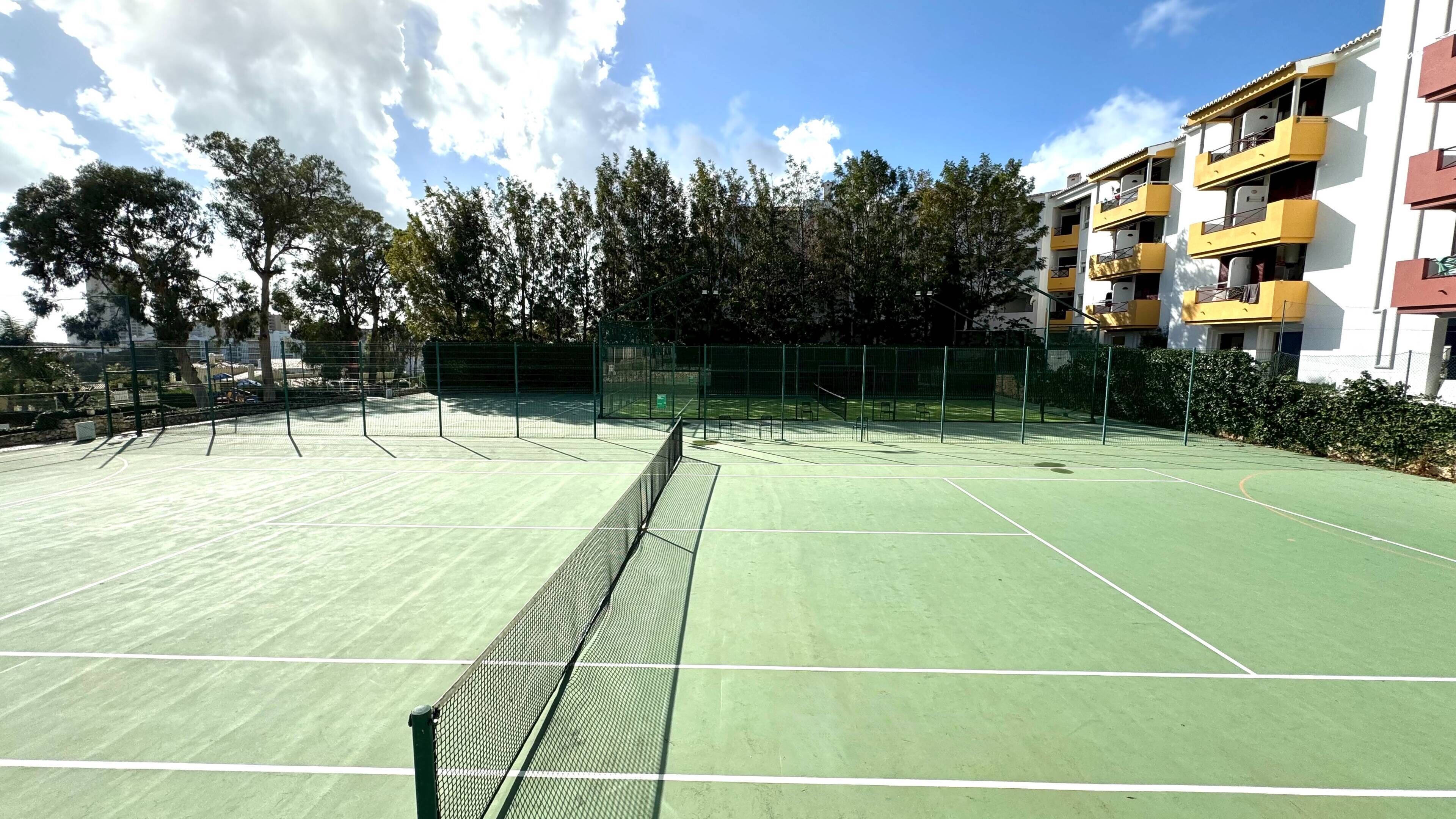 Ein Tennisplatz mit Netz, umgeben von Bäumen und einem Gebäude mit Balkonen.