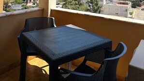Un balcón con mesa y sillas, vista a edificios altos y cielo despejado.