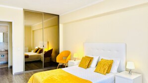 Habitación de hotel con una cama grande, un espejo, una silla y una mesita de noche con una lámpara.