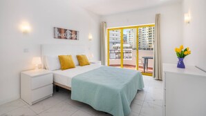 Une chambre d’hôtel moderne, équipée d’un lit, de tables de chevet, d’une fenêtre avec des rideaux et offrant une vue sur les bâtiments environnants.