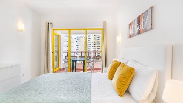 A hotel room with a bed, a nightstand, a window with curtains, and a view of the outside balcony.
