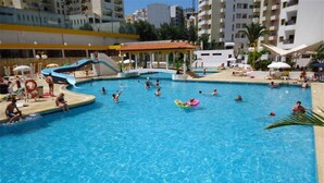 A swimming pool with a slide, lounge chairs, and a pavilion.