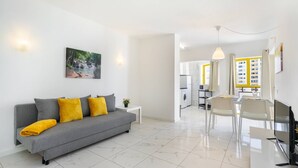 A modern living room with a grey sofa, yellow cushions, a small table with a plant, and a painting of a waterfall on the wall.