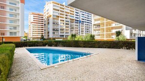 A swimming pool with a tiled deck, surrounded by a hedge and buildings in the background. - Praia da Rocha, 502 Faia, T1 by IG (Portimão)