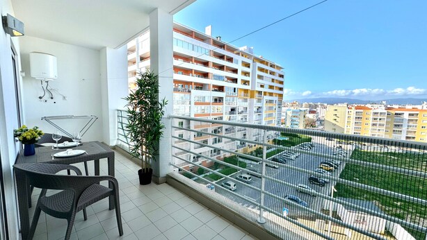 A balcony with a dining table, chairs, a potted plant, and a view of a parking area and buildings. - Praia da Rocha, 502 Faia, T1 by IG (Portimão)