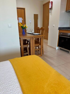 Une chambre d’hôtel comprenant un lit, une table à manger avec des chaises, un vase de fleurs et un coin cuisine avec une cuisinière.