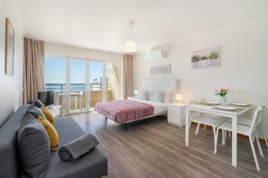 Una habitación de hotel moderna con cama, sofá, mesa de comedor con sillas, televisor y balcón con vista al mar.