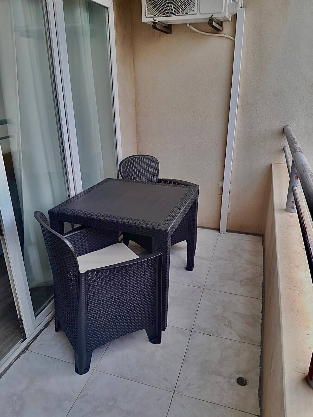 Un balcon avec une table et des chaises, un appareil de climatisation et une porte vitrée.