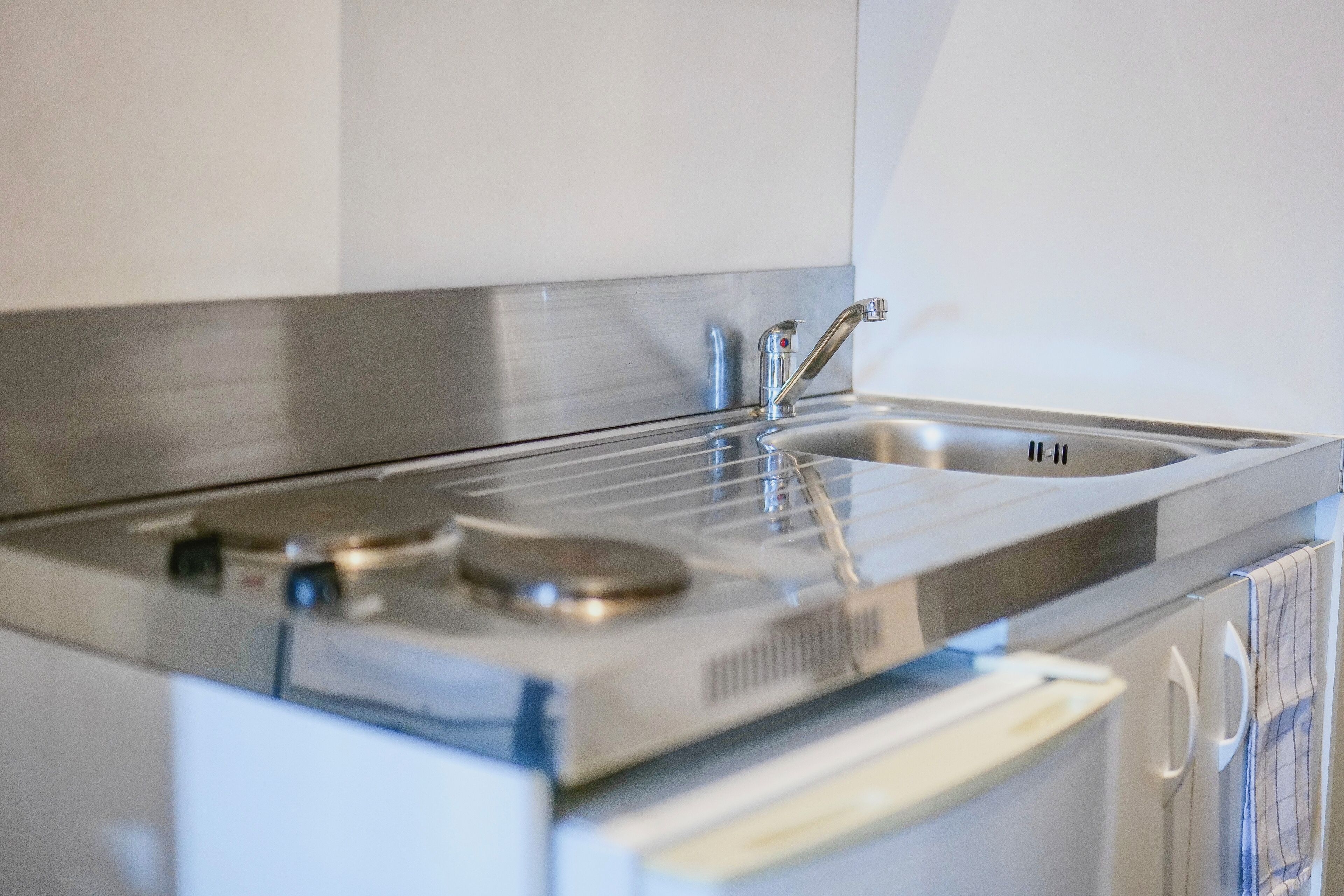 A kitchen with a stainless steel sink, a double faucet, and a built-in stove.