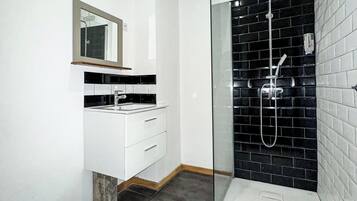 A modern bathroom with a toilet, a vanity with a mirror, and a glass-enclosed shower area with black tiles.