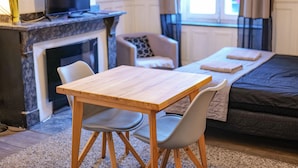 A cozy room with a wooden table and two chairs, a sofa, a TV, and a fireplace. - Les Cinq Lys (Carcassonne)