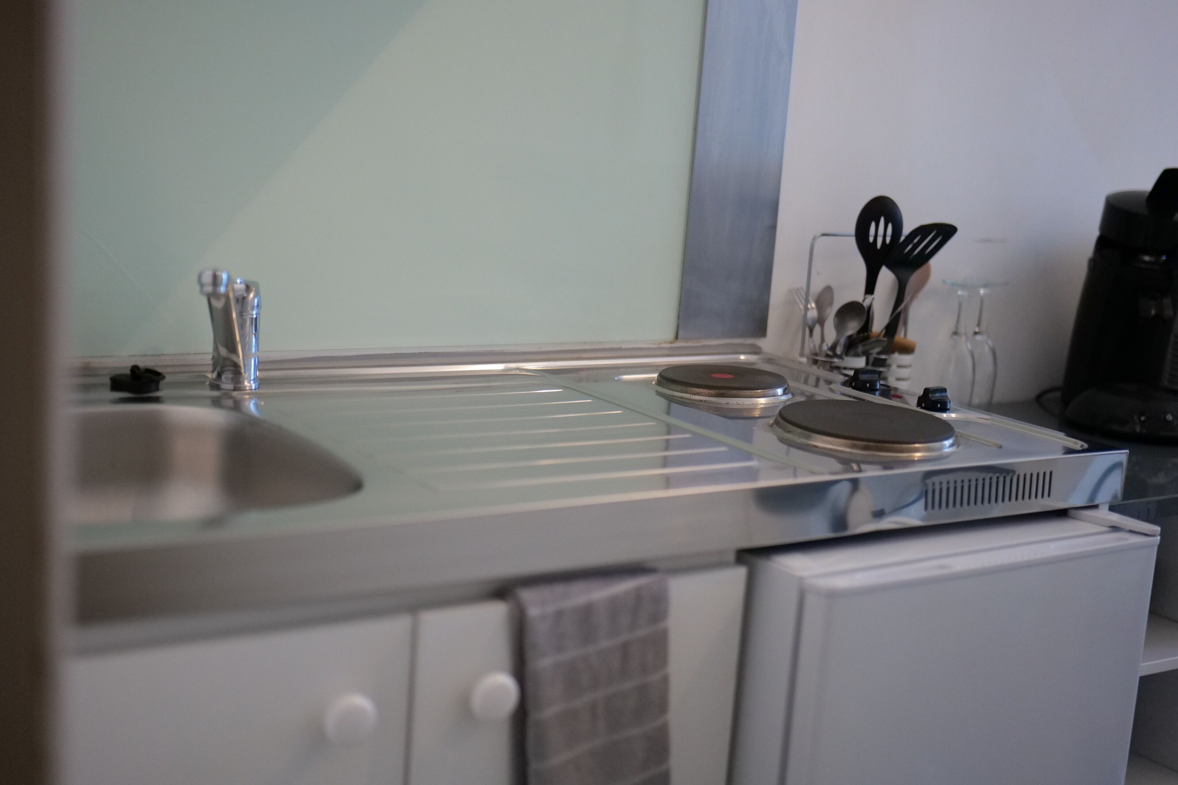 A kitchen with a stainless steel sink, a coffee machine, and various utensils.