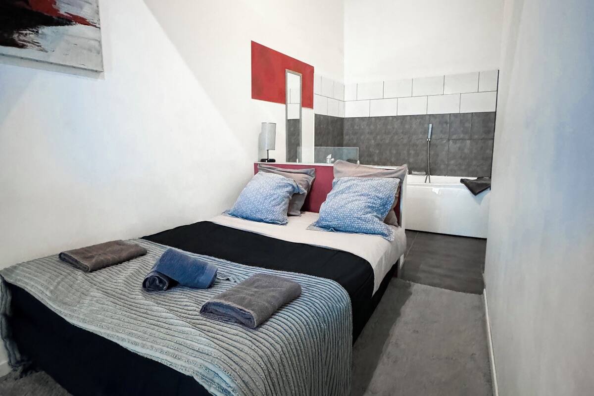 Una habitación de hotel moderna con una cama grande, un baño con bañera y una pared de acento roja.