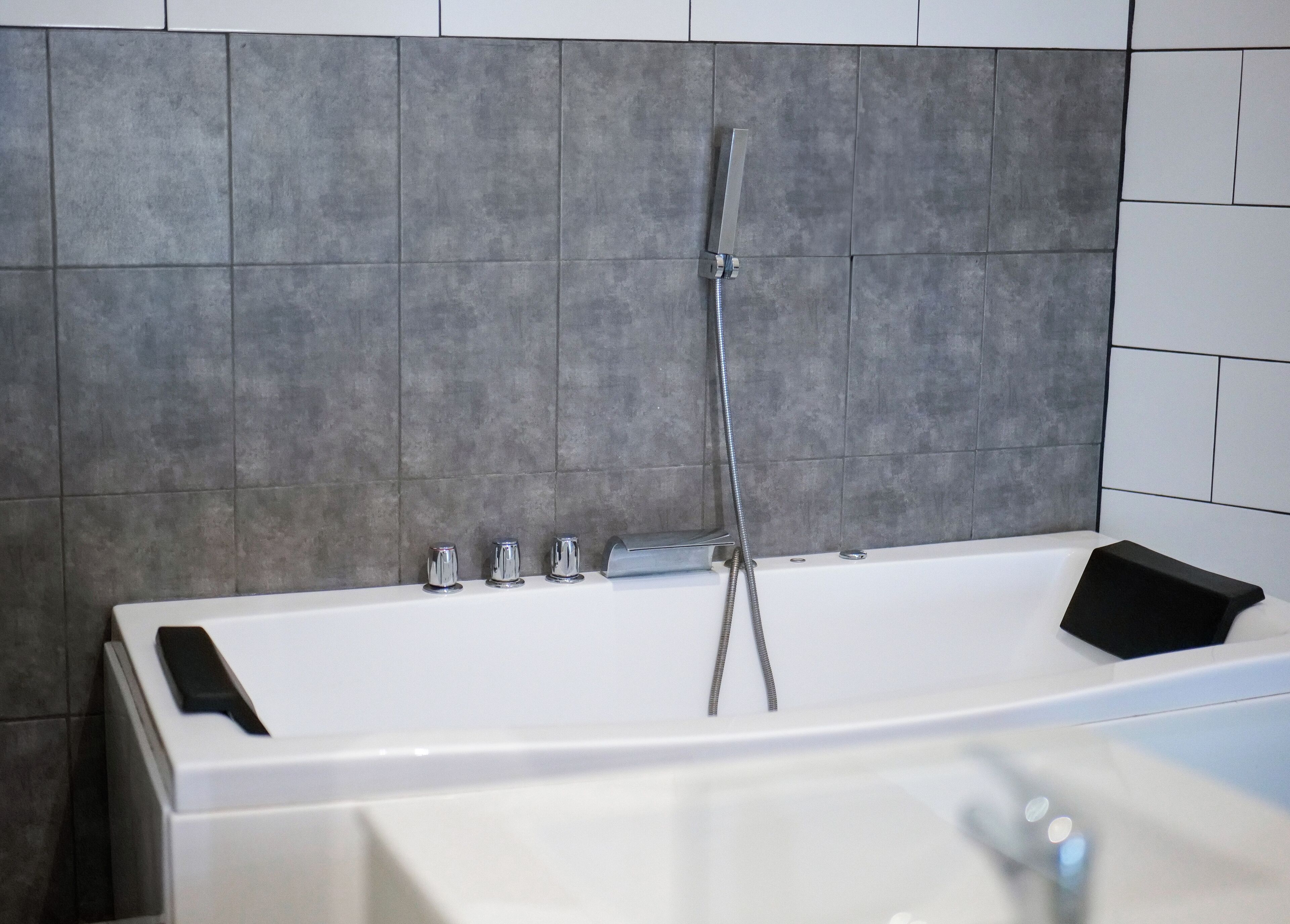 Une salle de bain moderne avec une baignoire, une douchette à main et un tapis de bain noir.