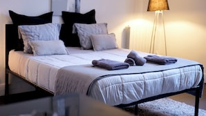 A neatly made bed with a white duvet, grey pillows, and folded towels. - Les Cinq Lys (Carcassonne)