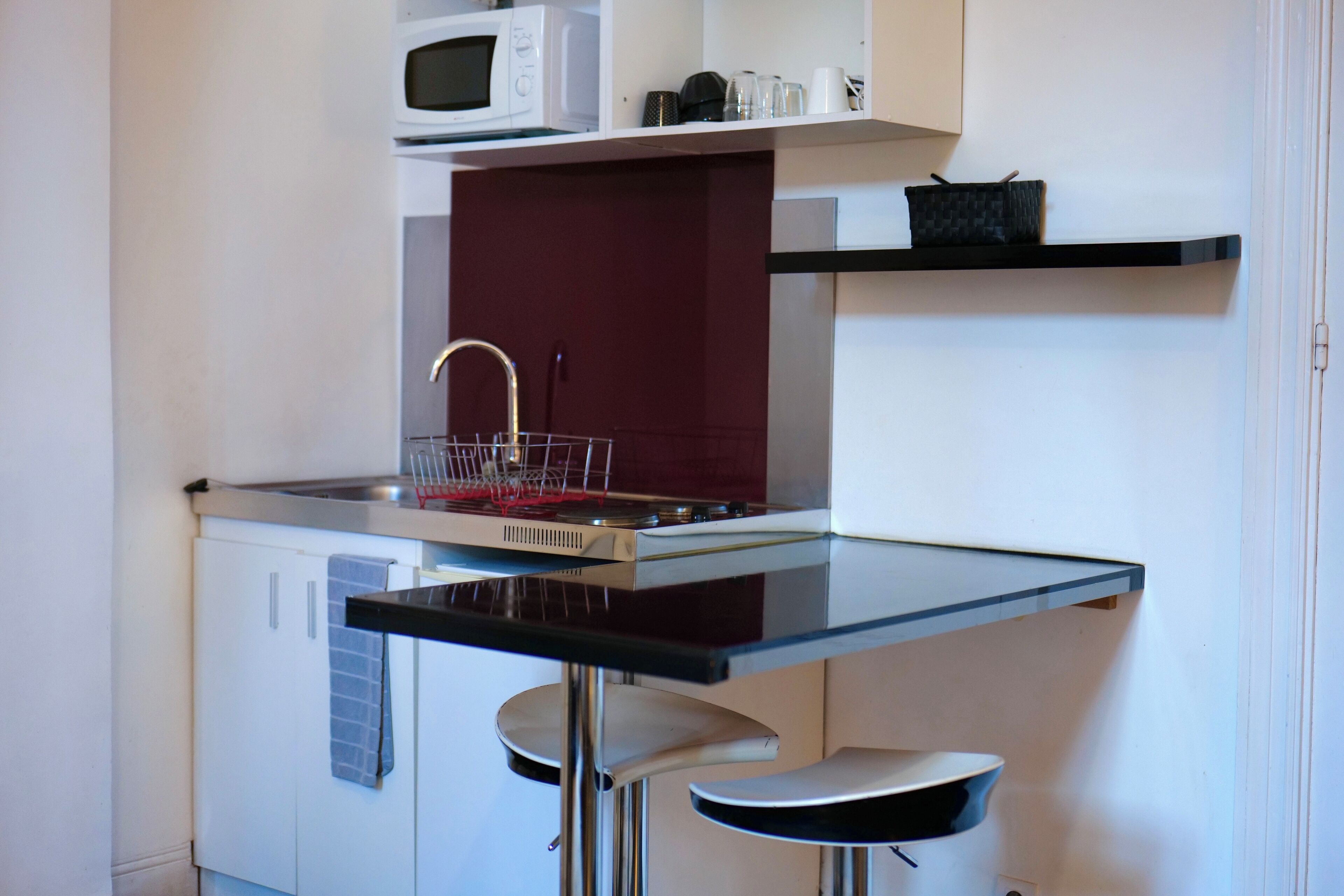 Una cocina compacta con microondas, pileta y dos taburetes de bar.
