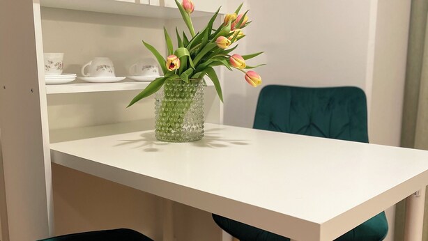 Ein Essbereich mit einem weißen Tisch, smaragdgrünen Stühlen und einer Vase mit Blumen.