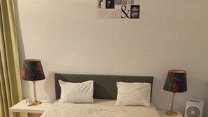 Ein ordentlich bezogenes Bett mit weißen Leinen und Kissen, zwei Nachttische mit Lampen, eine Wanduhr und ein kleiner Luftreiniger.