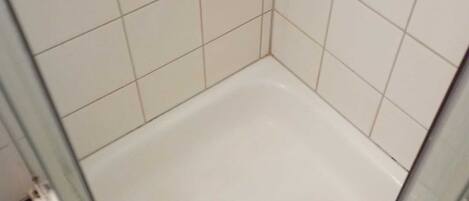A shower with white tiles, a glass door, and a red rug.