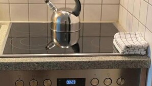 Eine Küche mit einem Herd, einem Wasserkocher und einer digitalen Uhr, die 08:23 anzeigt.
