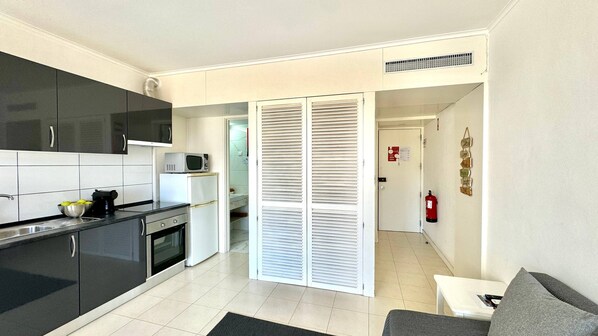 A modern kitchen with black cabinets, a white refrigerator, and a microwave. There is a small dining area with a table and a couch.
