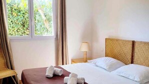 Ein Hotelzimmer mit Bett, Stuhl, Nachttisch mit Lampe und einem Fenster mit Vorhängen.