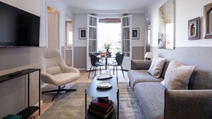 A modern living room with a sofa, armchair, flat-screen TV, dining table, and open windows. - CASA CALABRIA 2 BEDROOM 4 PAX (Barcelona)