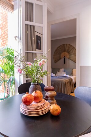 Un tavolo da pranzo con un vaso di fiori, piatti e un melograno. Si vedono un letto e una ventola sullo sfondo.