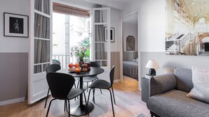 A modern living room with a dining area, open windows, and a large painting on the wall. - CASA CALABRIA 2 BEDROOM (Barcelona)