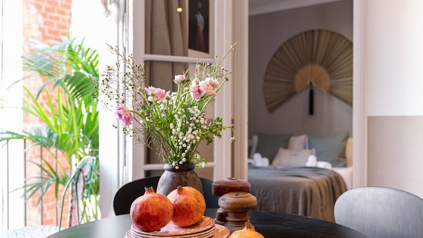 A dining table with a vase of flowers, pomegranates, and stacked plates. - CASA CALABRIA 2 BEDROOM (Barcelona)