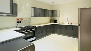 A kitchen with dark cabinets, a stove, a microwave, and a refrigerator. - Spacious & New 4-bedroom apartment in peaceful Madinah with AC, Fast-WiFi (Madinah)