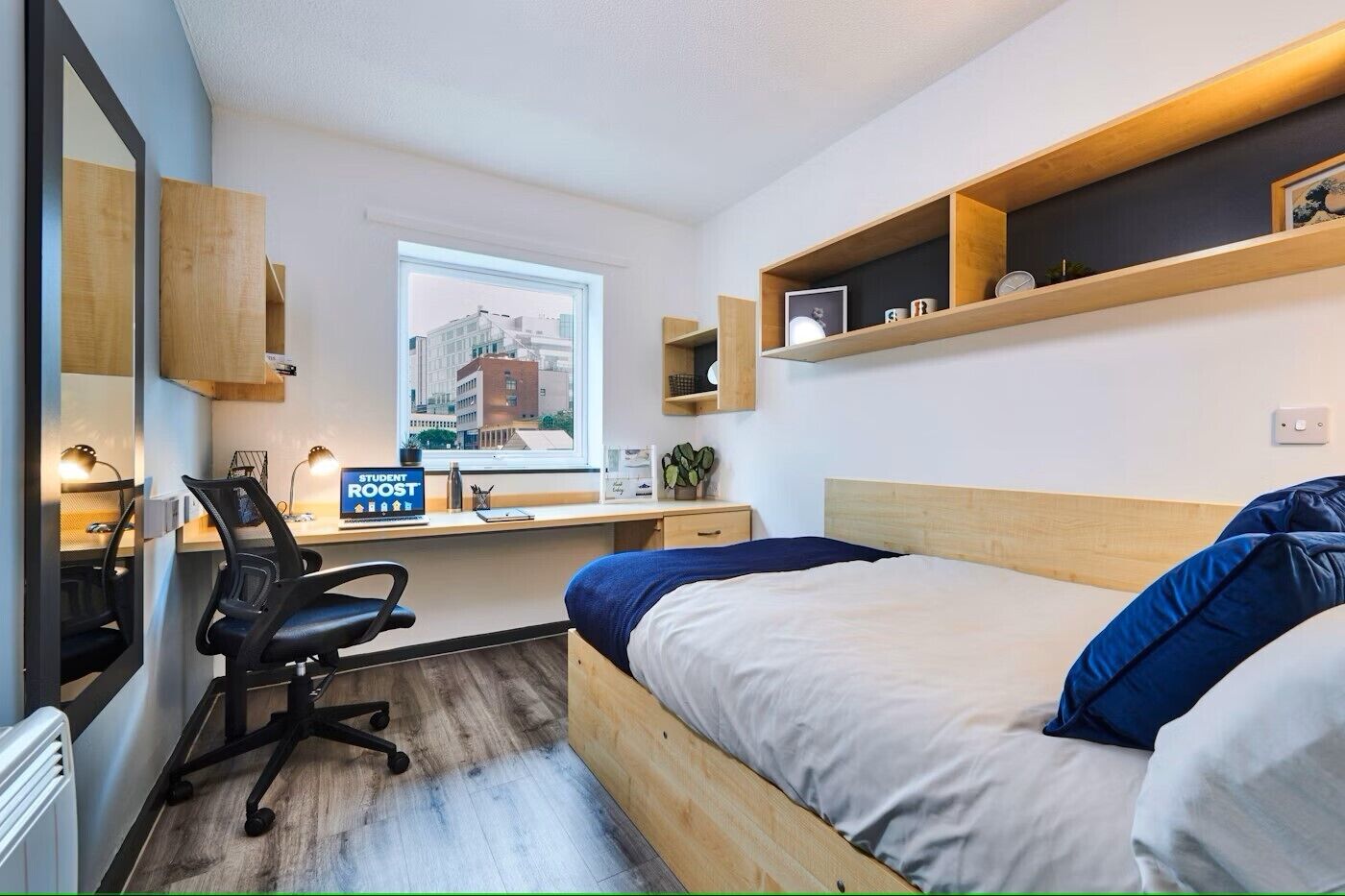 Un dormitorio moderno con una cama de madera, un escritorio con computadora, una silla y una ventana con vista a la ciudad.