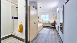 Une chambre d’hôtel moderne avec un plancher en bois, un lit, un bureau avec un ordinateur, une chaise et une fenêtre.