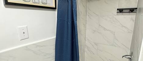 A bathroom with a shower, a framed picture on the wall, and a blue shower curtain.
