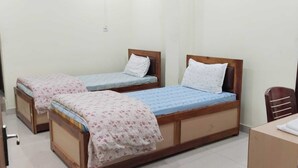 Una habitación con dos camas de madera, cada una con una almohada y una manta. Hay una silla de madera y una mesita con una toalla.